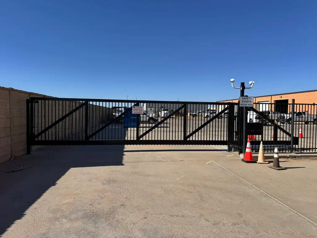 Long black picket cantilever slide gate closing an industrial yard entrance, fleet trucks and a metal building behind