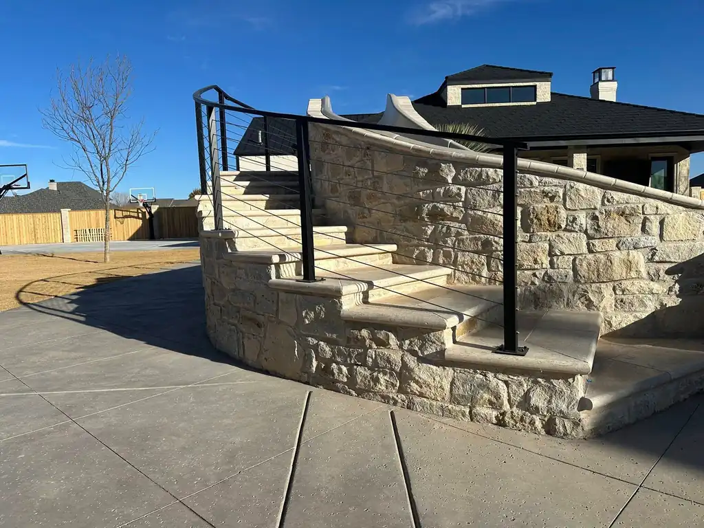 A curved cable-rail stair railing following a limestone garden wall