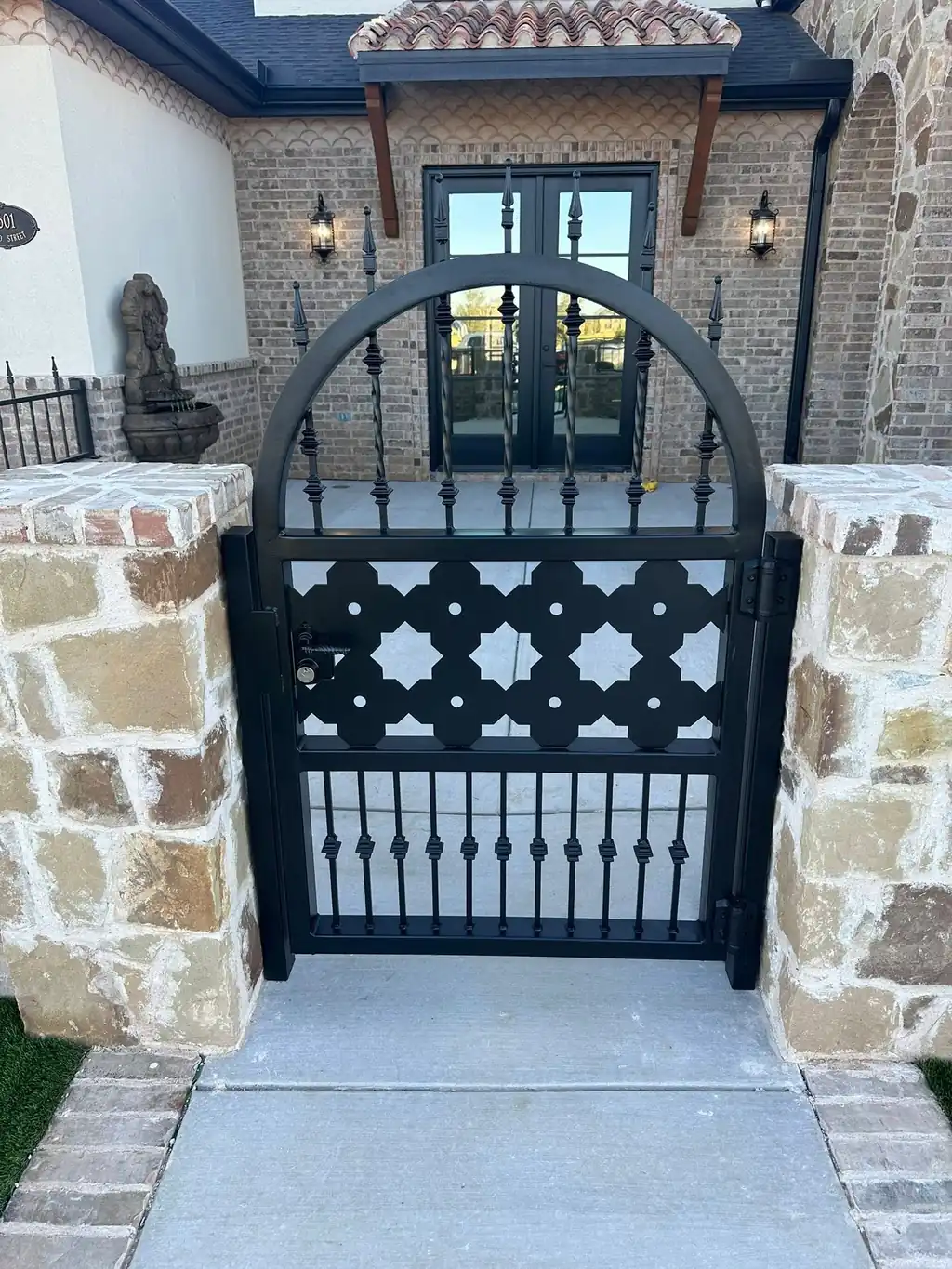 Arched ornamental pedestrian gate with a laser-cut star panel and twisted pickets, set between stone columns at a Lubbock home