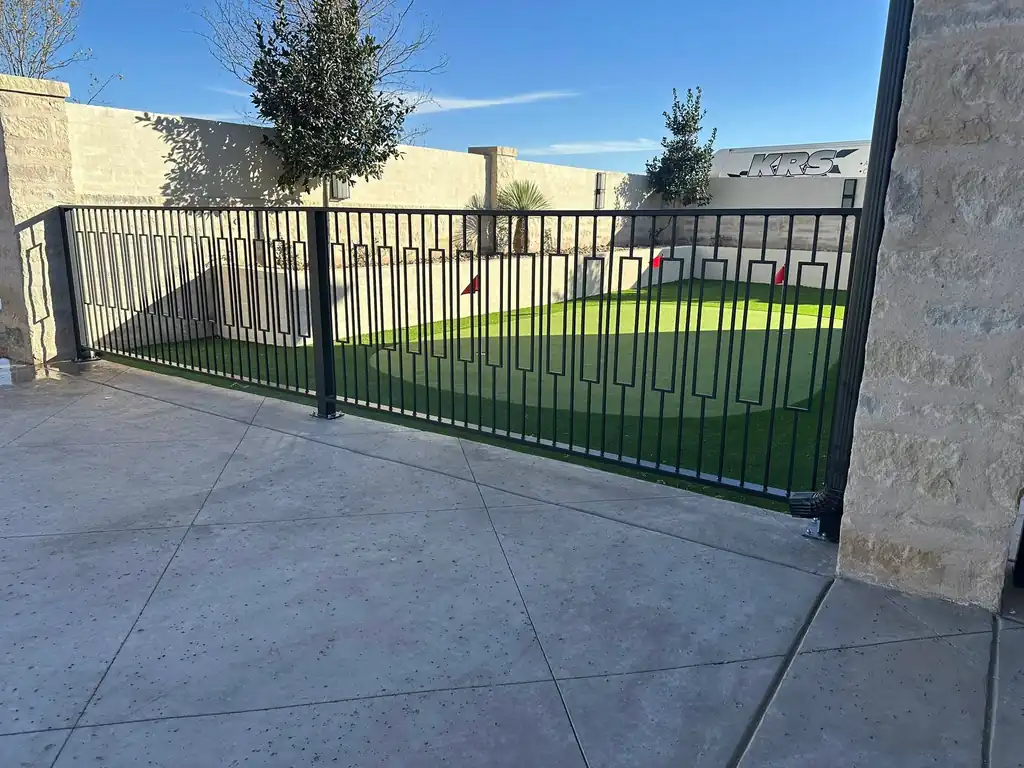 A decorative metal fence panel with a rectangular inset motif running above a putting green