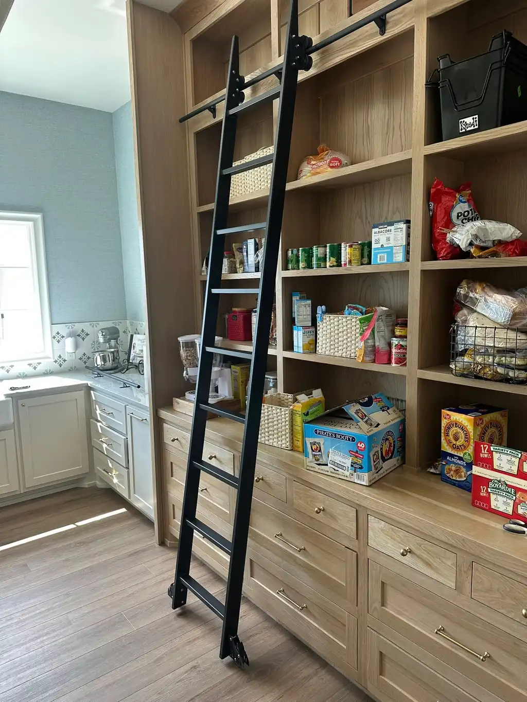 A black steel rolling library ladder on a rail, custom built for a homeowner's pantry