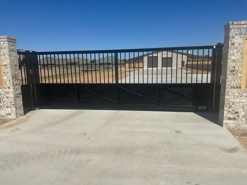 A black picket slide gate with X-braced lower panels between brick entry columns at a new-build home