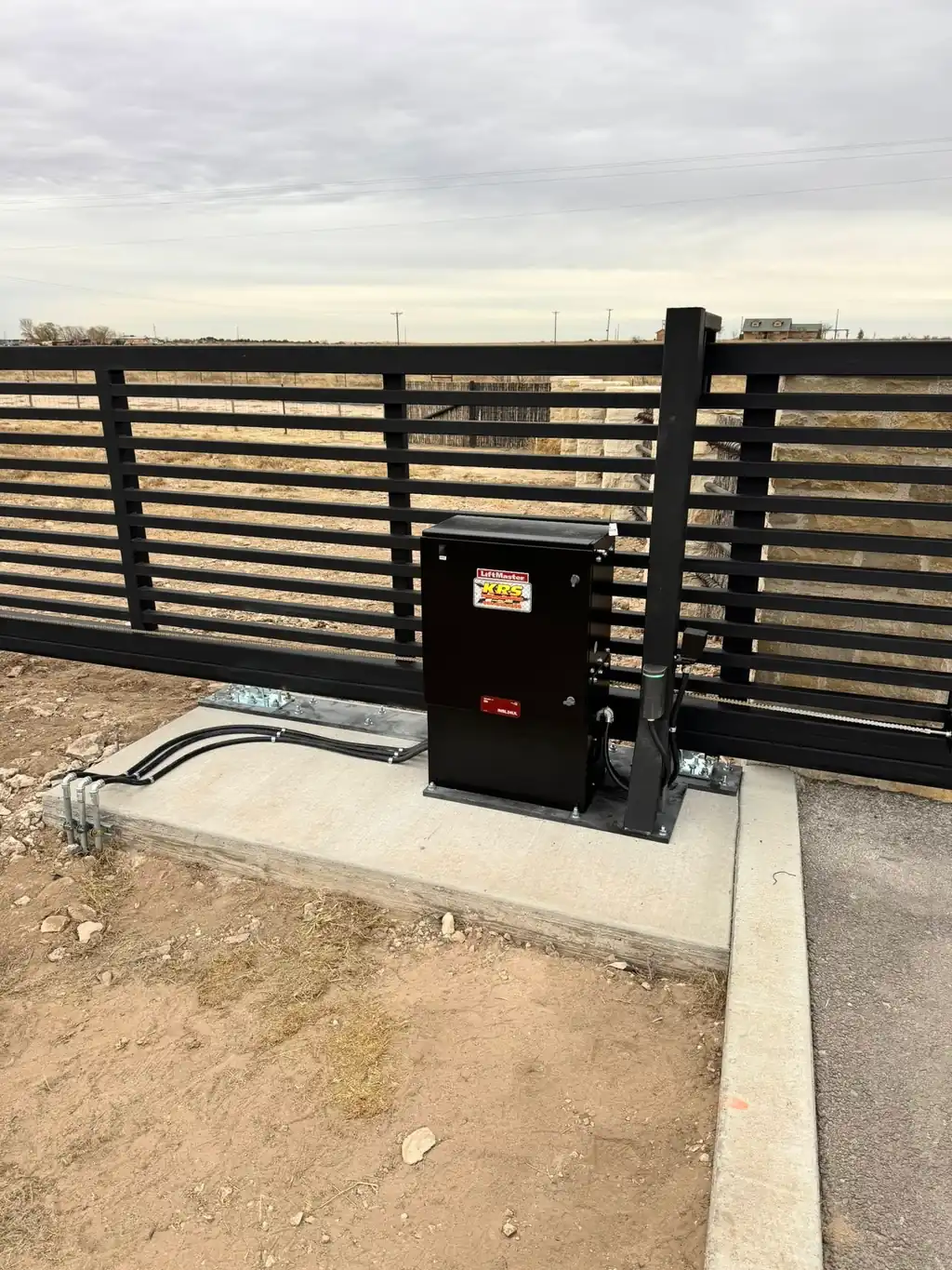 A LiftMaster gate operator with the KRS service sticker, mounted beside a slat gate