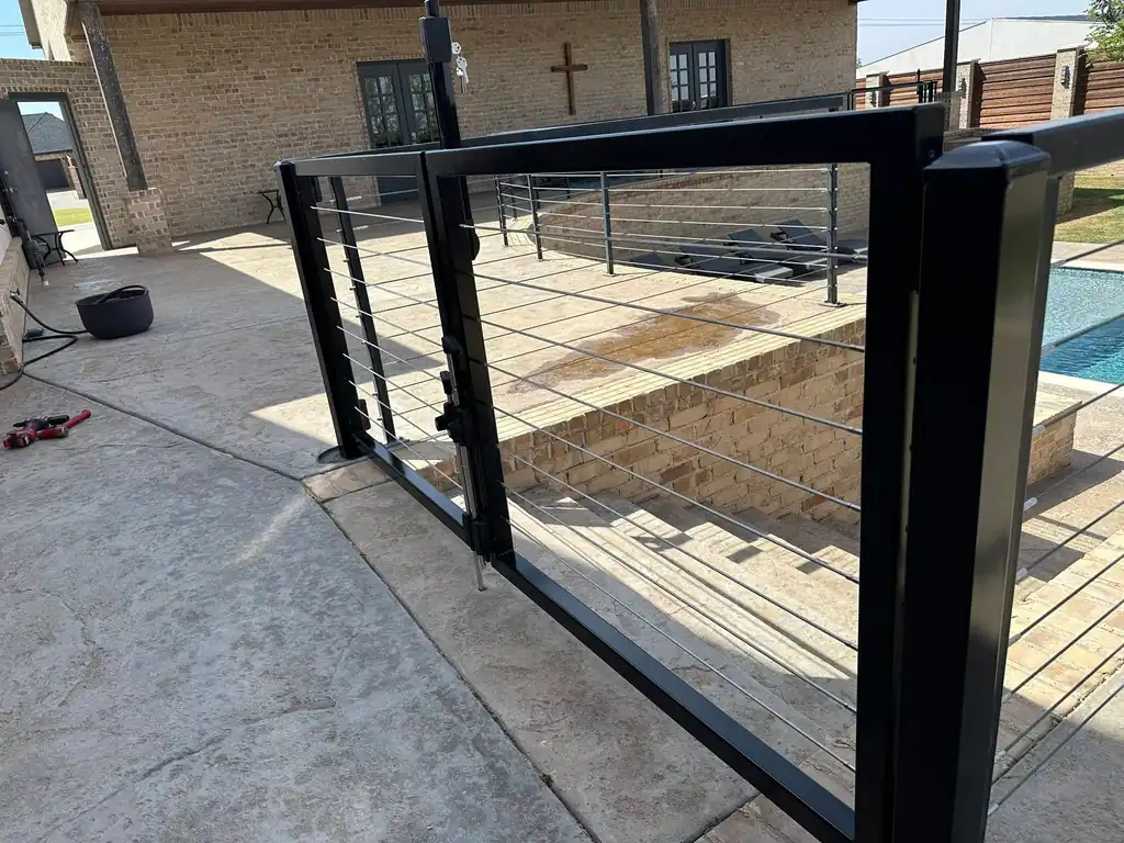 A black cable-rail pool gate and matching railing at a brick home